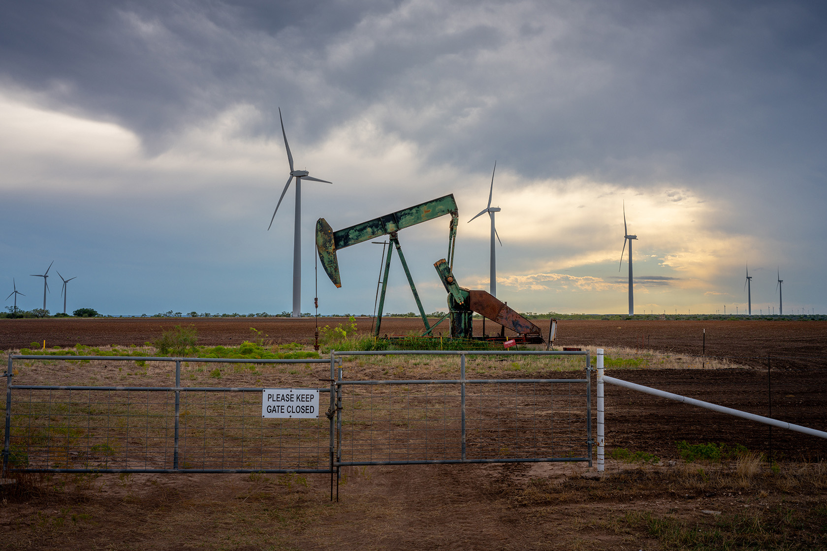 An oil pumpjack is seen near a field of wind turbines.