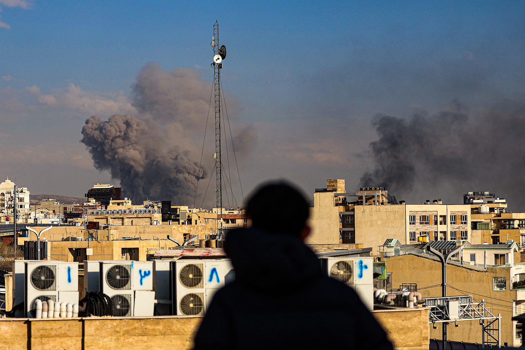 A person observes smoke rising in the distance after explosions were reported in Tehran.