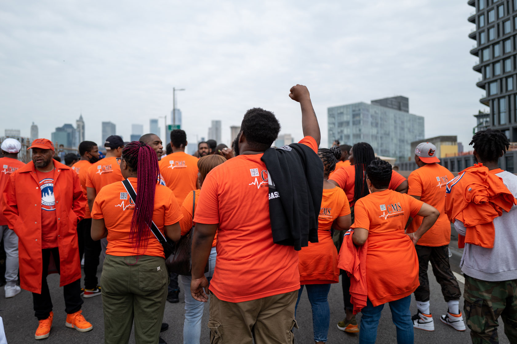A group of people stand gathered at a march to denounce gun violence. A man in the foreground raises his fist in the air.