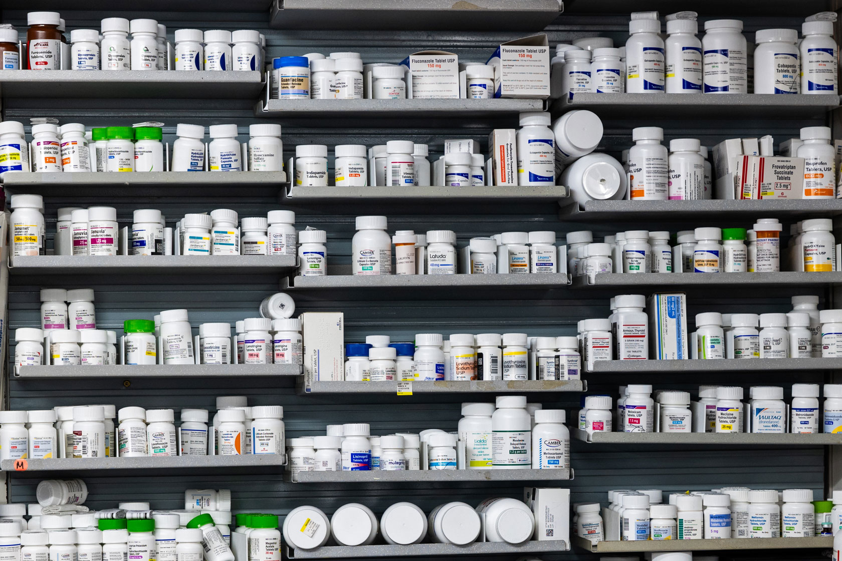 Shelves at a pharmacy are stacked with bottles of prescription medication.