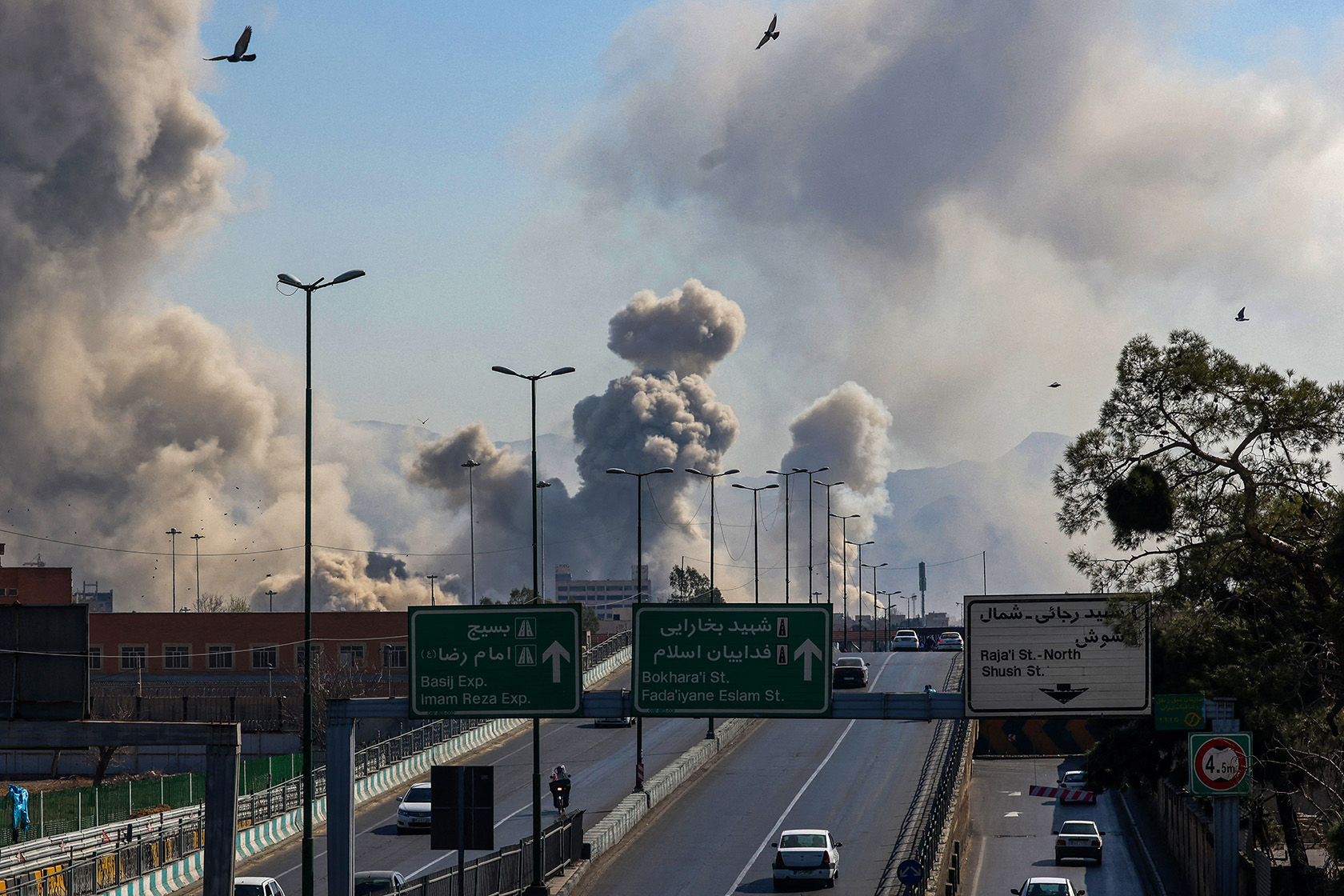 Motorists drive along an expressway as plumes of smoke rise after a strike in Tehran.