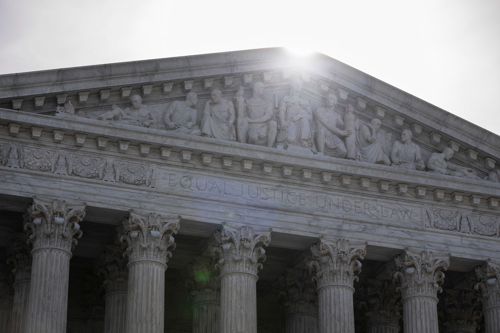 The sun appears to divide a facade while rising over the U.S. Supreme Court building.