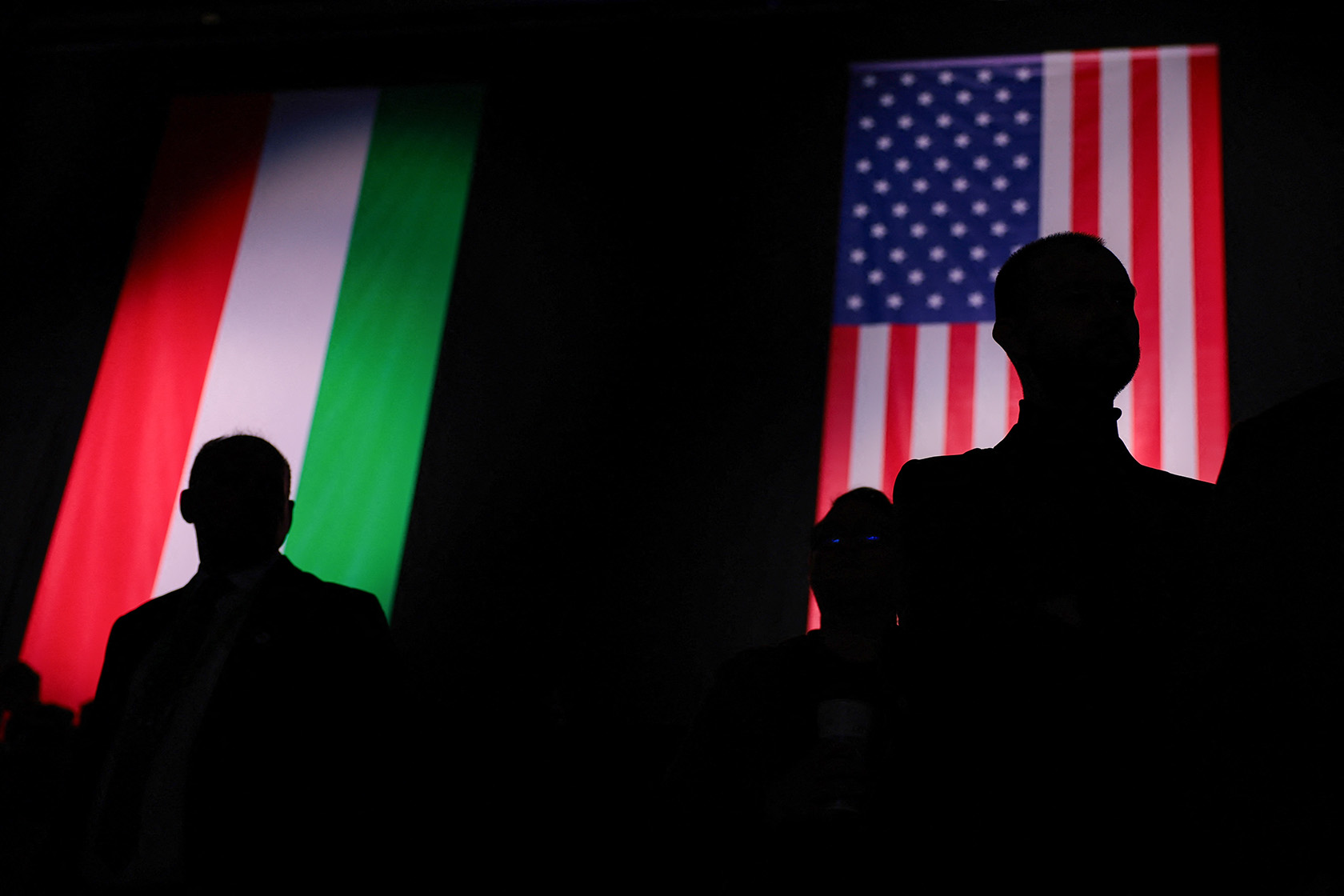 People stand silhouetted against a backdrop of the U.S. and Hungarian flags.