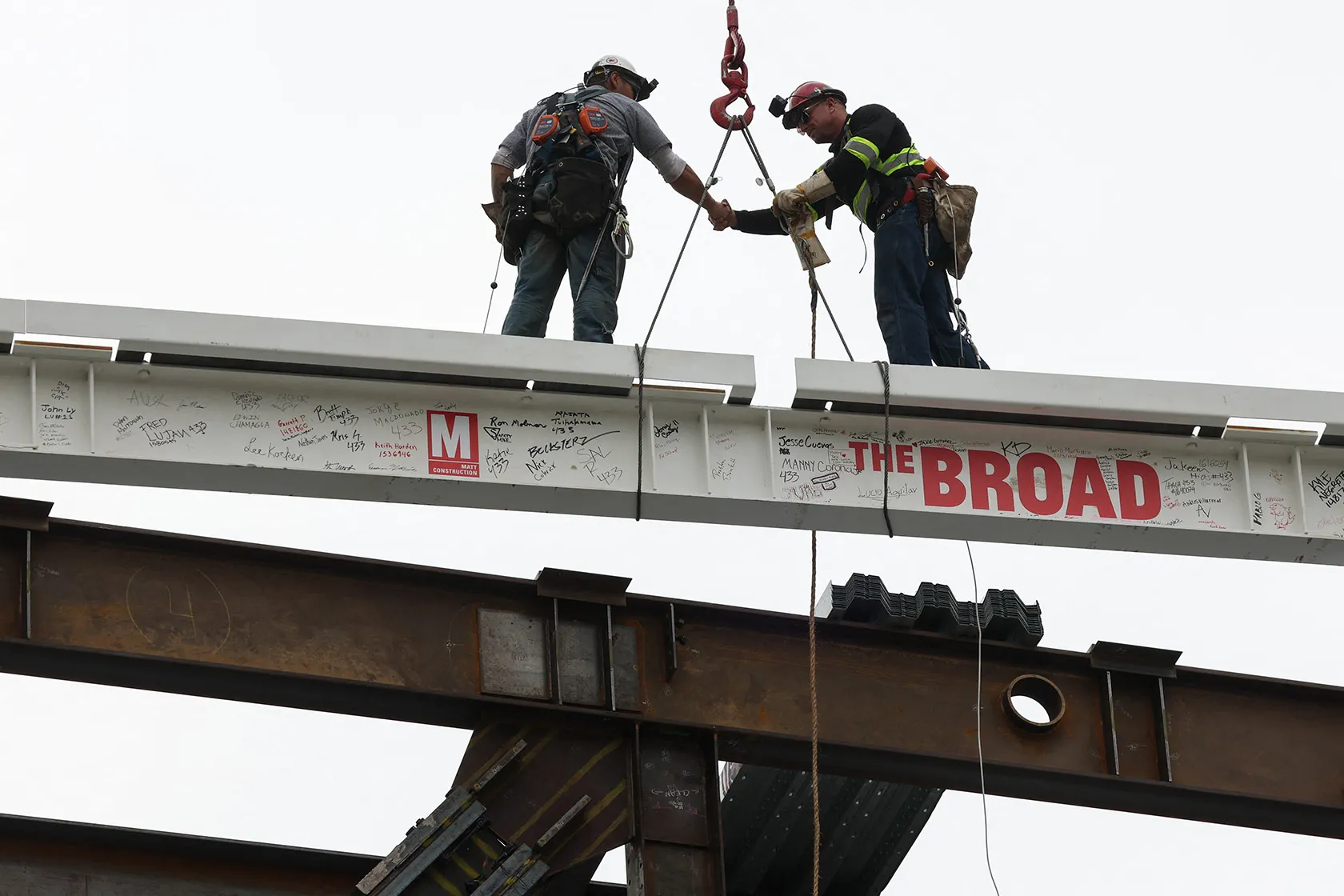 Workers shake hands while standing on a steel beam.