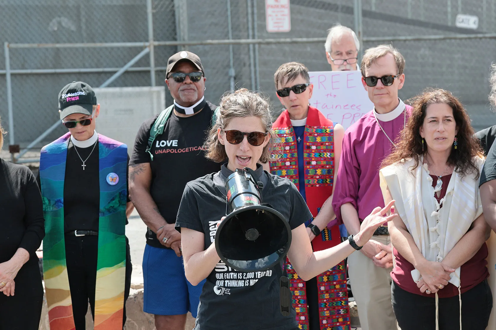 A group of faith leaders standing together. The person in front is holding a megaphone.