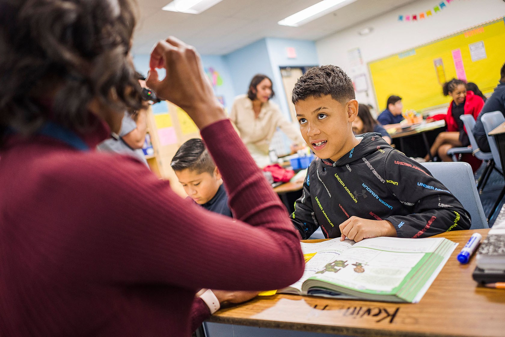 A teacher gestures while helping a student with schoolwork.