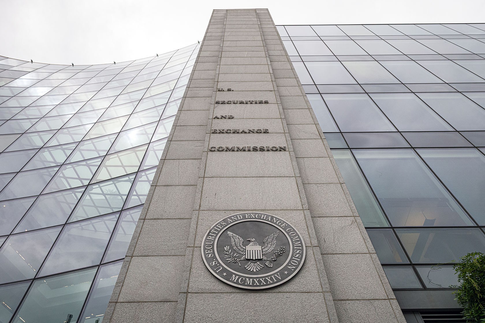 A curved glass facade and a flat glass facade flank a stone part of the building that has the agency's seal.