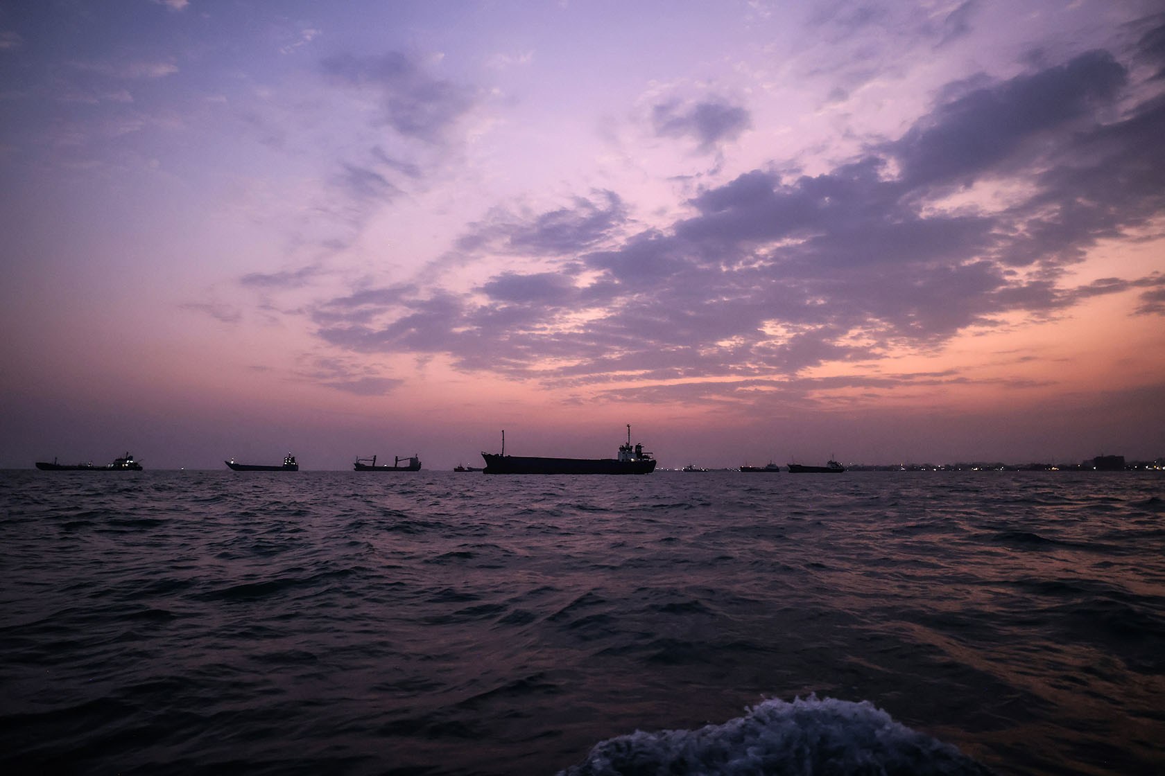 Several ships transit choppy waters under a purple and pink cloud-streaked sky.