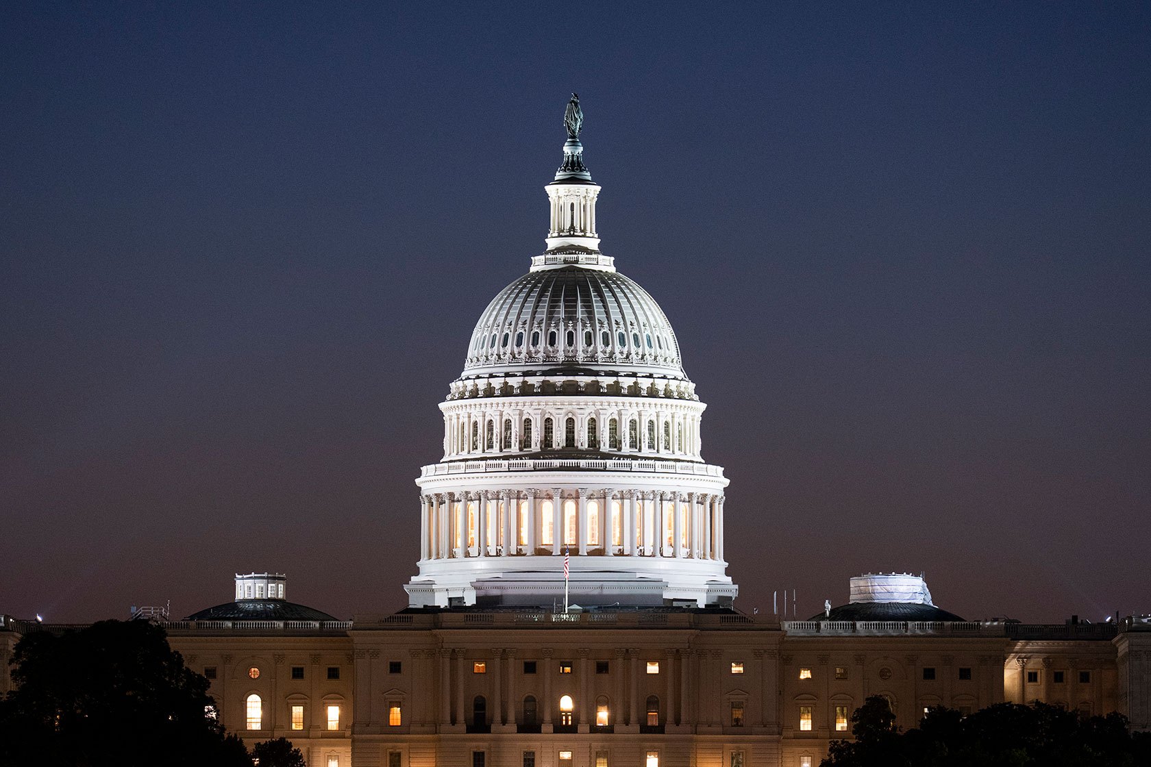 The illuminated dome of the U.S. Capitol, topped by the Statue of Freedom, against a pre-dawn sky
