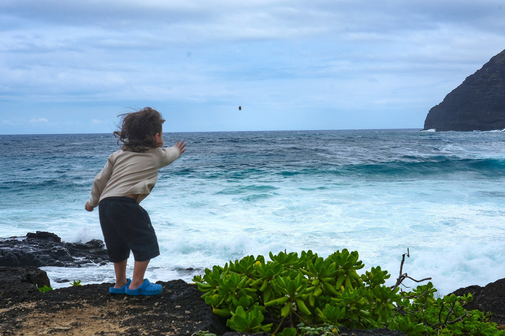A child throws a rock toward the ocean in Honolulu.