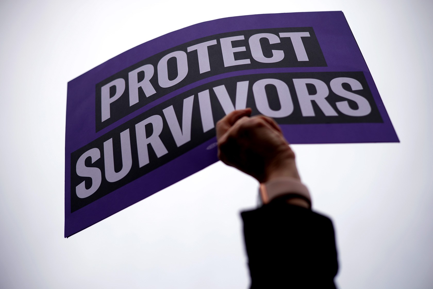 An activist holds up a sign that reads “Protect Survivors.”